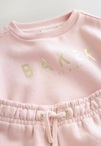 Miękki różowy zestaw bluzy i spodni dresowych z złotym logo "BAKER by Ted Baker" oraz ściągaczem w talii ze złotymi oczkami.