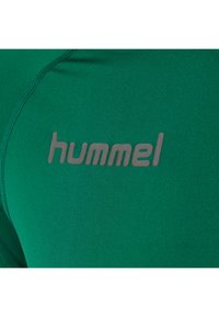 Groene sportshirt met een gestructureerde stof en een groot grijs "hummel" logo op de voorkant, dat een schone en moderne uitstraling benadrukt.