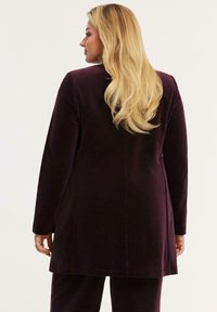 Lange mouwen, diep paarse jas van zacht materiaal met een rechte snit, met strakke lijnen en minimale details.