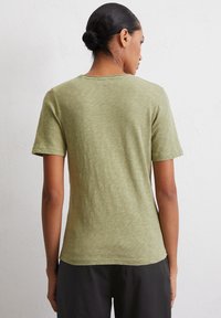 T-shirt a maniche corte di colore verde oliva realizzato in un tessuto morbido e testurizzato. Presenta un collo rotondo e semplici dettagli di cucitura. Vestibilità standard.