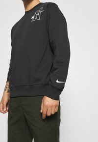 Sudadera negra con cuello redondo, que presenta un logo impreso en blanco en el pecho y un swoosh blanco en la manga. Tejido suave.