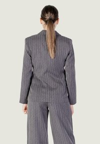 Completo grigio a righe con maniche lunghe e vestibilità su misura. La parte posteriore presenta una fessura singola ed è abbinato a pantaloni larghi coordinati.