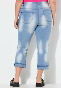 Pantalones capri de denim de lavados claros con un patrón descolorido, con puños enrollados y dos bolsillos traseros. Combinados con unas sandalias negras con detalles dorados.