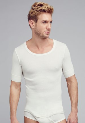 Weißes, geripptes T-Shirt mit kurzen Ärmeln, weitem Ausschnitt, figurbetontem Design und glatter Textur, getragen von einem Modell vor einem grauen Hintergrund.