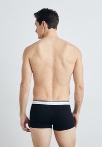 Boxeri negri cu un elastic alb și negru cu dungi. Materialul pare neted, aderând strâns în jurul șoldurilor.