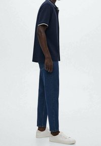 Polo navy con dettagli bianchi, abbinato a jeans blu a gamba dritta e sneakers bianche, che presenta un look casual e moderno.