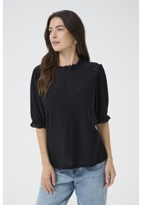 Top nero realizzato in tessuto testurizzato, con maniche a sbuffo, scollatura volant e motivi a occhiello. Abbinato a jeans in denim azzurro chiaro.