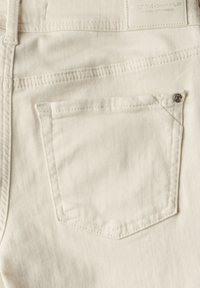 Tessuto di denim bianco con una tasca sul retro con dettagli di cucitura. Piccolo rivetto metallico in accentuazione all'angolo della tasca. Etichetta in vita.