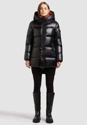 Black puffer jacket with a shiny finish, hood, zip front, and a brown interior lining. Paired with a black knit skirt and knee-high boots.