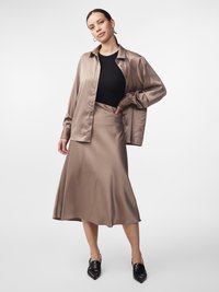 Satijnen beige blouse, aansluitend zwart topje en bijpassende vloeiende rok. Zwarte puntige schoenen en oversized oorbellen maken de look compleet.