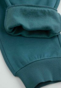 Turkusowe dresy z miękkim, szczotkowanym wnętrzem, ściągaczami na mankietach i gładkim zewnętrznym materiałem o lekko elastycznej fakturze.