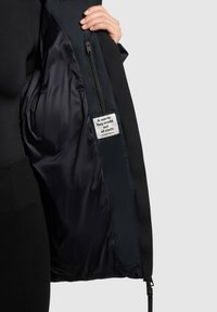Black jacket with a smooth, shiny inner lining. Features a zip pocket and a fabric label stating "A warm hug made out of cloth."
