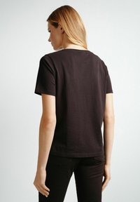 Czarna bawełniana koszulka z klasycznym okrągłym dekoltem i krótkimi rękawami, wyeksponowana z tyłu, z gładką teksturą i prostym wzorem.