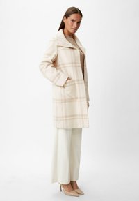 Cappotto in misto lana color crema con un leggero motivo a quadri, dotato di colletto a rever, tasche laterali e una vestibilità rilassata. Abbinato a pantaloni chiari.
