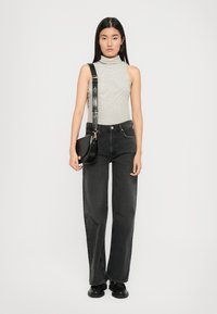Black wide-leg jeans paired with a gray striped turtleneck top. Model holds a small black crossbody bag with a curved design and strap.