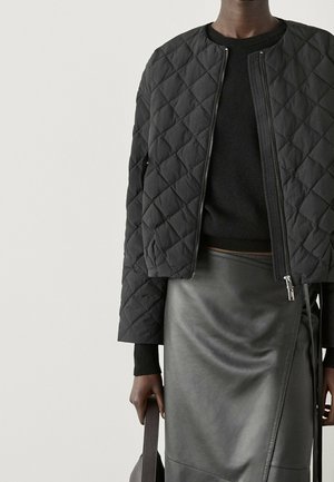 Kurtka bomber w czarnym pikowaniu z zapięciem na suwak, zestawiona z czarnym swetrem i dopasowaną skórzaną spódnicą, uzupełniona szarym torbą.