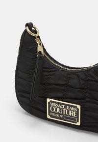 Svart nylonaxelväska med textur som är sammanknuten, guldfärgad metall, dragkedja som stängning och en varumärkeslogoplåt framtill.