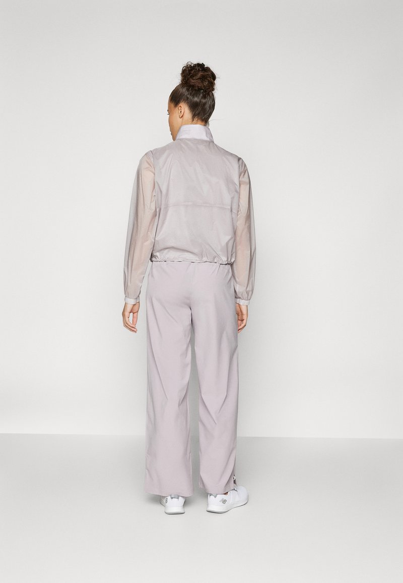 Leichte, halbtransparente graue Jacke mit elastischem Saum und Bündchen, kombiniert mit weiten lavendelfarbenen Hosen und weißen Sneakern.