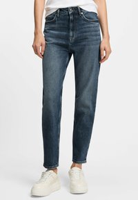 Donkerblauwe denim jeans, high-waisted, met een rechte pijpdesign, voorzien van ton-sur-ton stiksels en een klassieke vijf-pocket stijl, gecombineerd met witte sneakers.