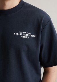 Navy blauwe katoenen T-shirt met een ronde ribgebreide kraag en witte tekst: "Mare D'Polo Denim BELLA CIAO FROM NAPOLI" aan de voorkant.