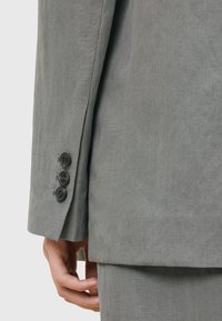 Ärmel eines grauen Anzugjackets mit glatter Textur und drei schwarzen Knöpfen am Bündchen, sichtbaren Nähten und maßgeschneiderten Passformdetails.