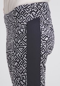 Svarta och vita mönstrade byxor med en mjuk, blank yta. Har en enfärgad svart sidodel och en figursydd design.