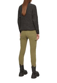 Olijfgroene cargobroek met taps toelopende pijpen en zijzakken, gecombineerd met een donkergrijze gebreide trui. Zwarte chunky laarzen maken de look compleet.