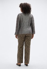 Szürke, hosszú ujjú, függőleges csíkos blúz, fekete és barna cikk-cakk mintás nadrággal párosítva, fekete magassarkú szandállal viselve.