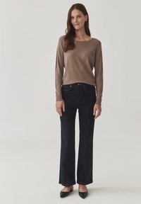 Lichtbruine longsleeve top, donkere spijkerbroek met uitlopende pijpen, zwarte schoenen met spitse neus. Soepele textuur, aansluitend ontwerp en klassieke kleuren.