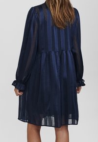 Granatowa sukienka w paski z marszczoną talią, długimi bufkami i falbanianymi mankietami; wykonana z przejrzystej, lekkiej tkaniny o subtelnym fakturowaniu.