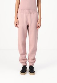 Pantalones deportivos rosas con cintura acanalada, puños elásticos y una textura suave, combinados con zapatos deportivos negros con suelas de goma.