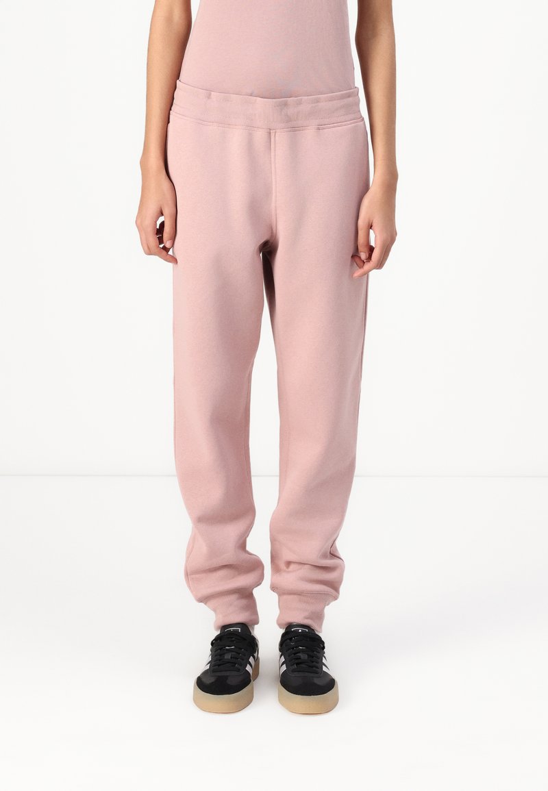 Pantalones deportivos rosas con cintura acanalada, puños elásticos y una textura suave, combinados con zapatos deportivos negros con suelas de goma.