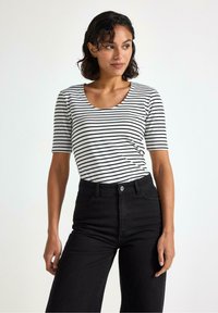 Kortærmet top med sort-hvide vandrette striber, der har en rund halsudskæring og blødt stof, parret med højtaljede sorte jeans.