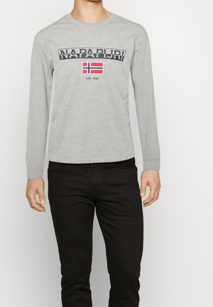 Mand iført grå langærmet skjorte med teksten "NAPAPIJRI", norsk flag og tryk med "EST. 1987", kombineret med sorte bukser.