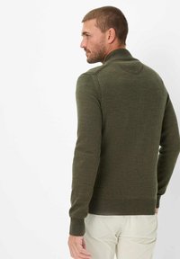 Dunkelgrüner Pullover mit hohem Kragen, gerippten Bündchen und Saum, aus strukturierter Strickware gefertigt. Sichtbares Schulternahtdetail.