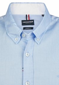 Lichtblauw overhemd met knopen en een moderne pasvorm. Voorzien van een puntige kraag, een witte binnenkraag en kleine logo-accenten nabij de knopen.