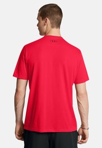 Camiseta roja de manga corta hecha de tejido suave con cuello redondo. Presenta un pequeño logo negro en la parte trasera del cuello y un ajuste relajado.