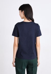 T-shirt en coton bleu marine avec un col rond et des manches courtes ; texture lisse et design simple, porté avec un pantalon vert.