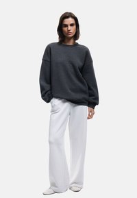 Ciemnoszara, oversize bluza z obniżonymi ramionami, w połączeniu z białymi spodniami o szerokich nogawkach. Miękka tekstura materiału, prosty krój i jednolite kolory.