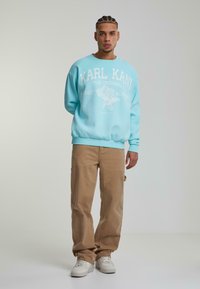 Felpa azzurra chiara con testo e grafiche bianche, abbinata a pantaloni cargo beige e sneakers bianche, che mostrano una vestibilità rilassata.