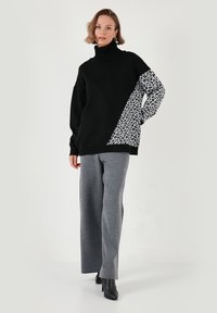 Pulover negru cu guler înalt, având un mânecă cu un print animalier gri și negru. Asortat cu pantaloni largi gri și cizme negre până la gleznă.