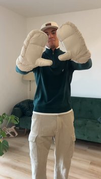 Luvas almofadadas bege com bordas arredondadas, apresentando um exterior texturizado e forro macio contrastante, usadas por uma pessoa com um suéter escuro.