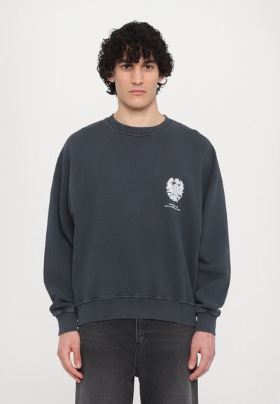 Sudadera de gran tamaño en gris oscuro con puños y dobladillo acanalados, que presenta un diseño gráfico blanco en el área del pecho izquierdo.