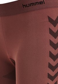 Tight-fit, mid-rise leggings in a muted reddish-brown. Features black chevron patterns along the side and a ribbed waistband with branding.