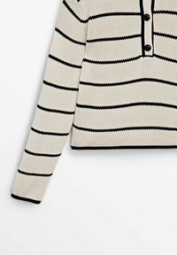Pull en maille blanc avec des rayures horizontales noires, manches longues, col boutonné et bordure noire aux poignets et à l'ourlet.