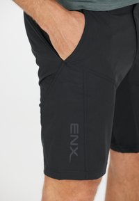 Schwarze Sportshorts mit Seitentasche, glatter Textur und kantigen Nahtdesigns. "ENX"-Logo auf dem unteren Bein gedruckt.