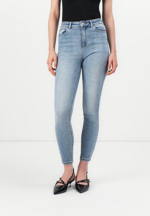 High-waisted, light blue skinny jeans with a smooth texture, featuring five pockets and a stitched waistband. Paired with black heels.