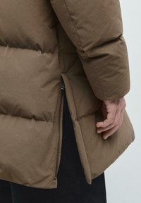 Giacca puffer marrone con finitura testurizzata, design trapuntato, zip laterale e orlo posteriore leggermente allungato.
