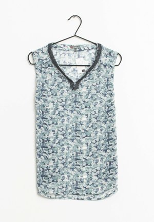 Blouse sans manches avec motif abstrait bleu-gris et bordure en V ornée de perles noires, suspendue sur un cintre noir contre un fond blanc.