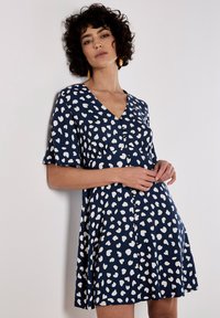 Marineblaues Kleid mit weißen herzförmigen Mustern, V-Ausschnitt, kurzen Ärmeln und Knopfdetails vorne, aus leichtem Stoff.